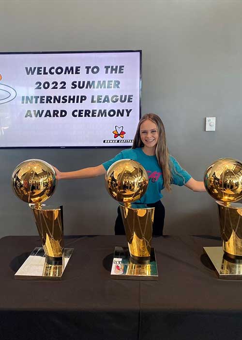 UF Online sport management and tourism, hospitality and event management student Kalena Miles poses with the  Miami Heat’s NBA championship trophies from 2006, 2012 and 20213.
