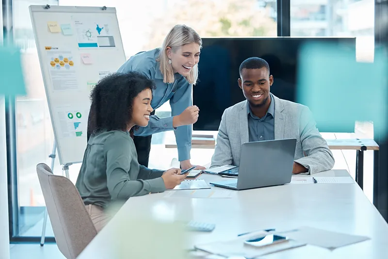 Three people smiling while grouped around computer screen.