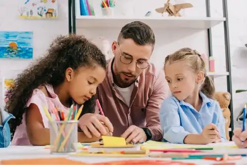Teacher seated at table with two children instructing them.